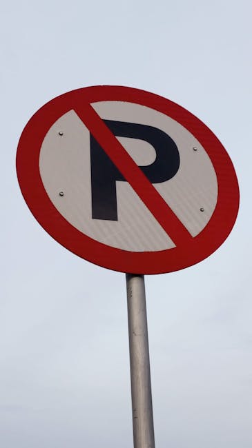 A round, red-bordered no parking sign with a blue background and a red diagonal line, mounted on a metal bracket attached to a red brick wall. The wall features horizontal rows of bricks in various shades of reddish-brown, with light gray mortar between them. The sign is positioned slightly to the left of the center of the image, with the wall extending evenly across the frame. Natural lighting illuminates the scene, highlighting the texture of the bricks and the reflective surface of the sign. This image relates to parking restrictions, which are relevant for home relocations and moving services in Southwark, as managed by Man with Van Denmark Hill, particularly when dealing with parking suspensions or fines associated with house removals.